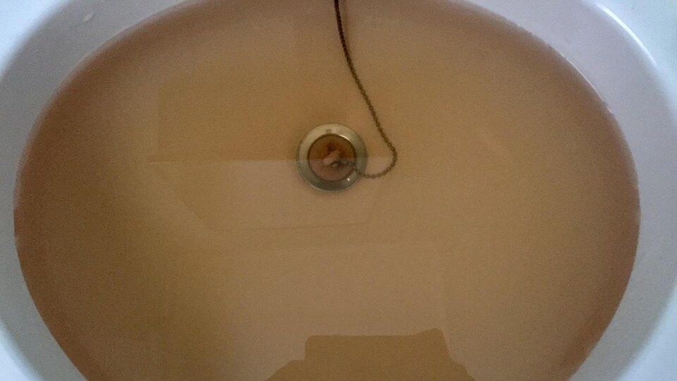 Évier de salle de bain rempli d'eau de couleur brun pâle.