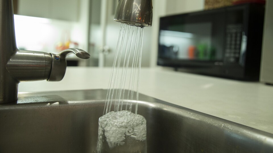 De l'eau coule d'un robinet d'un évier de cuisine dans un verre.