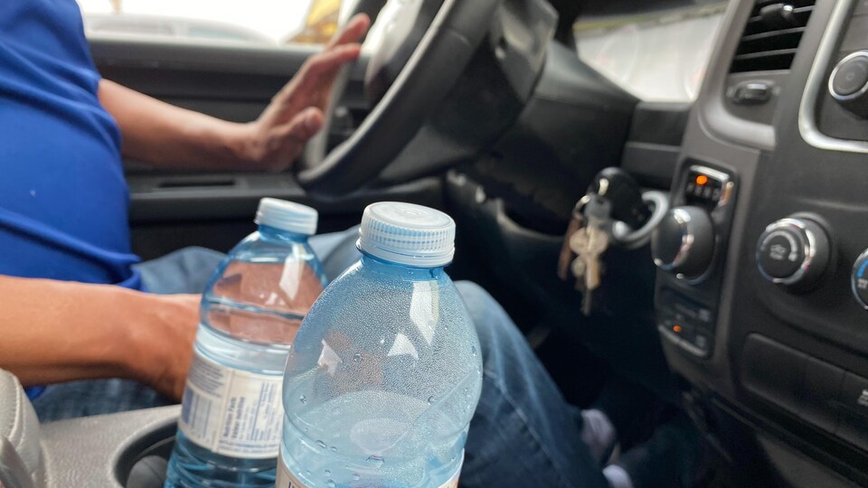 Deux bouteilles d'eau posées dans une auto avec en fond, les mains d'un homme qui conduit.
