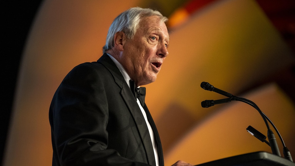 Un homme parle au micro derrière un lutrin lors d'un gala.