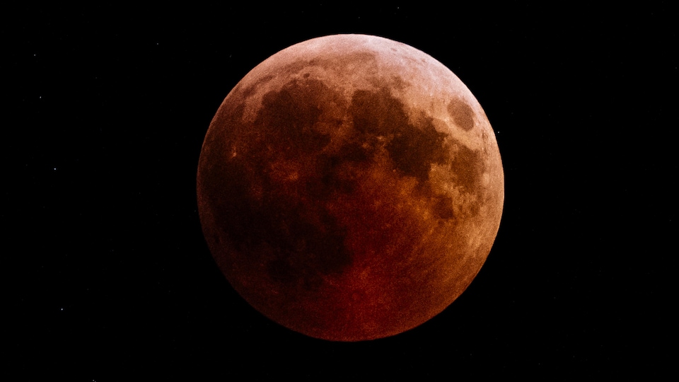 La Lune, pleine, est rougeâtre à cause de la réflexion de la lumière du Soleil par l'atmosphère terrestre.