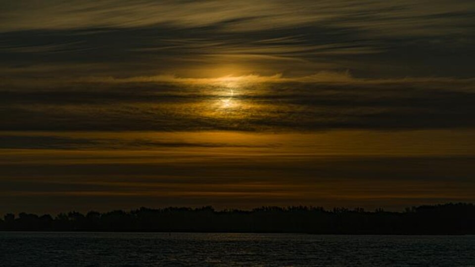 Le Soleil se lève sur le Saint-Laurent tandis que la Lune en cache une partie.
