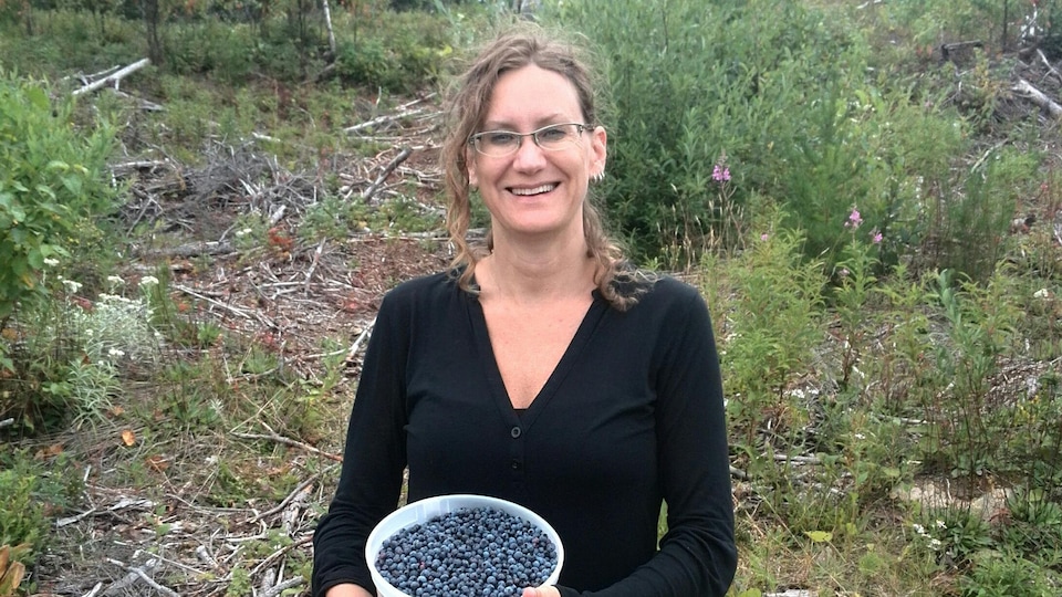 Une femme dans la nature tient un contenant rempli de bleuets.