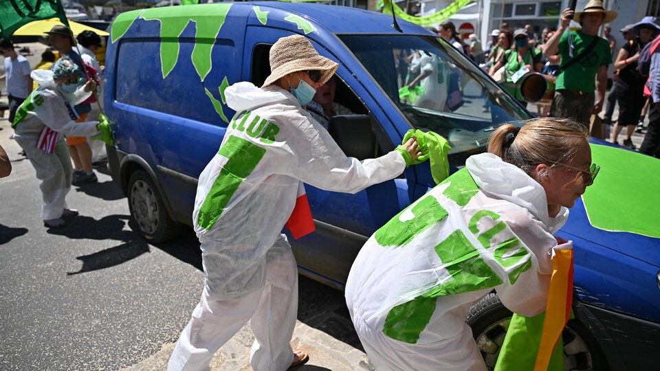 Des manifestants lavent symboliquement un véhicule coloré de vert.