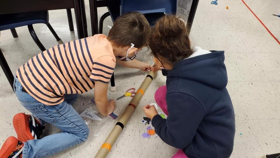 Des enfants en train de faire un bricolage avec un tube de carton.