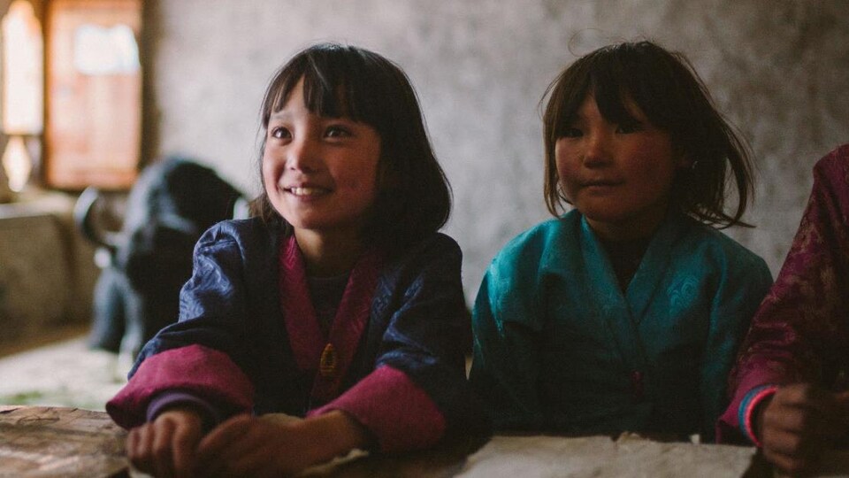Deux jeunes filles sourient dans une salle de classe, avec un yak couché en arrière-plan.