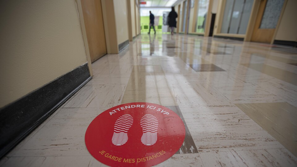 Un couloir d'une école avec, sur le sol, des consignes de distanciation.