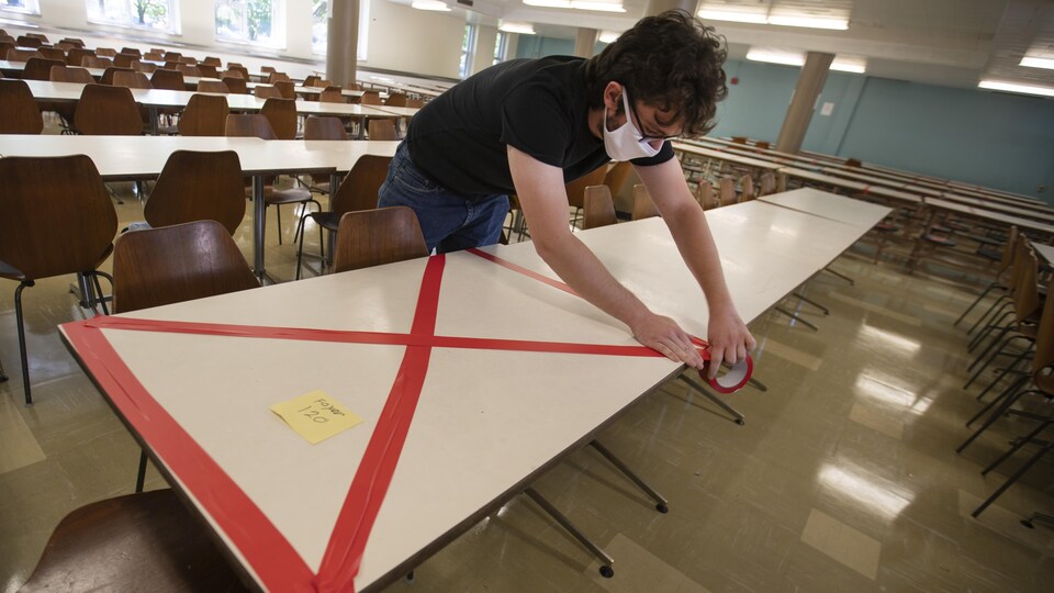 Un homme met du ruban rouge sur une table d'un cafétéria d'une école.