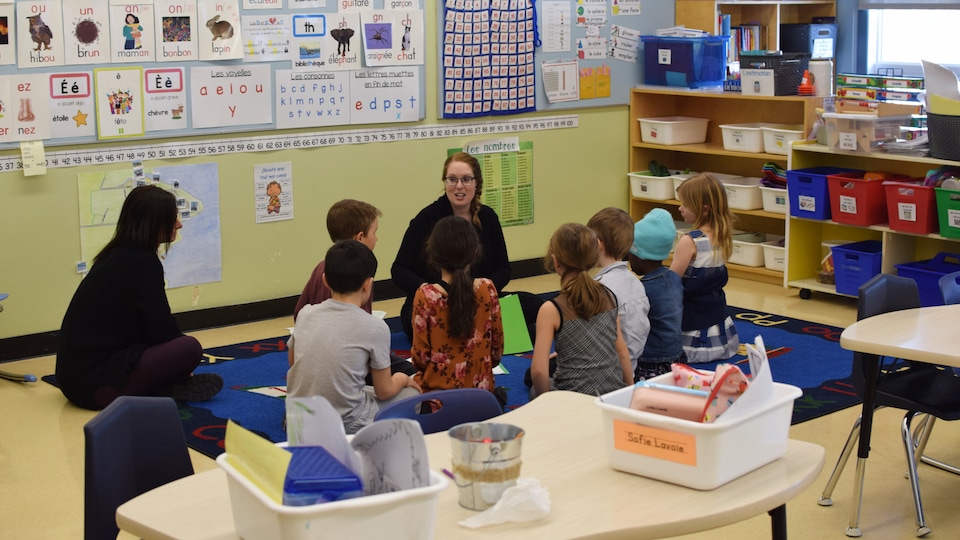 Une enseignante s'adresse à des enfants assis par terre autour d'elle dans une salle de classe.