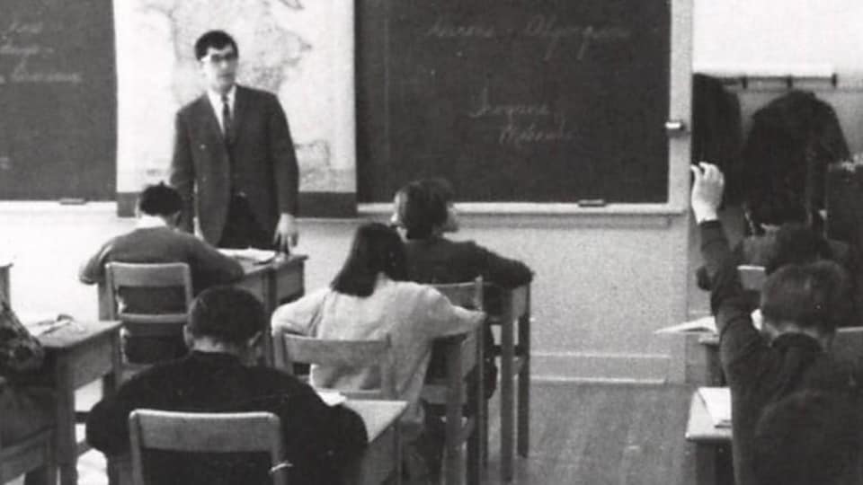 Un enseignant se tient debout devant une classe sur une photo d'archive usée et prise en noir et blanc.