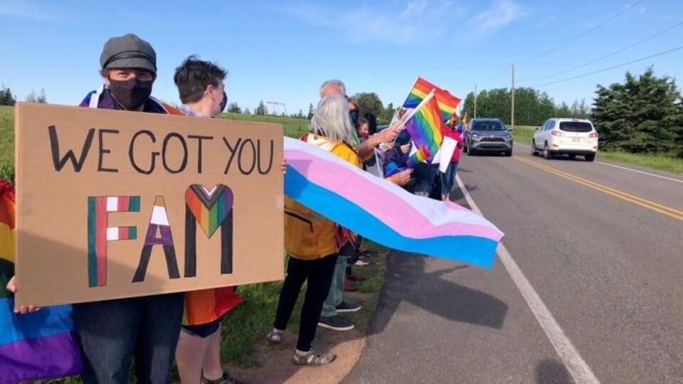 Plusieurs manifestants portent le drapeau de la Fierté, l'arc-en-ciel au bord de la route.