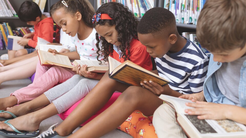 Des enfants assis devant une étagère lisent des livres.