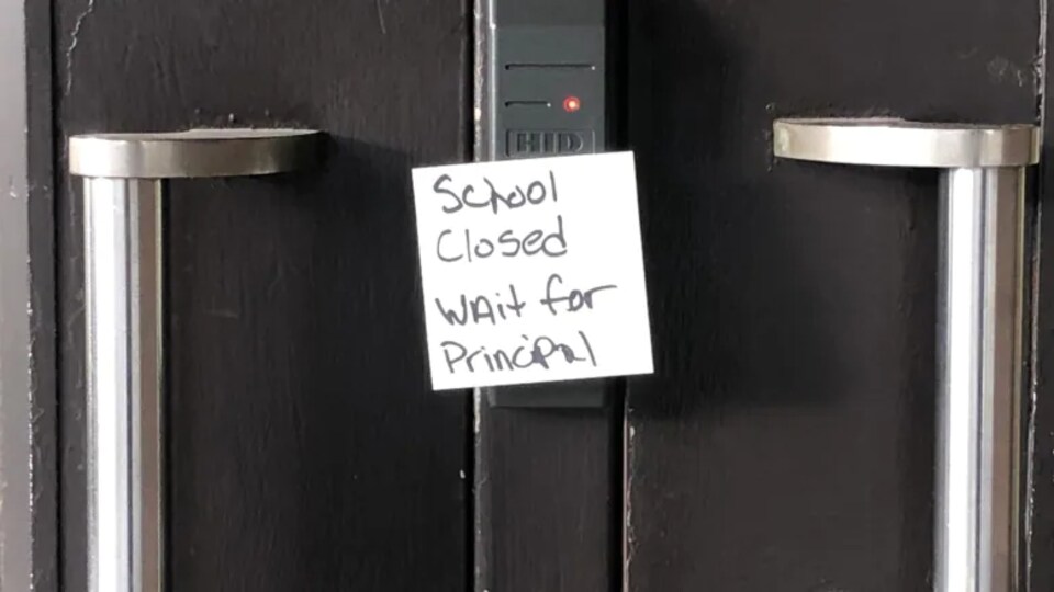 Les portes d'une école sont barrées avec un écriteau "école fermée, attendre le directeur".