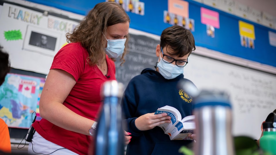 Une enseignante regarde un dictionnaire larousse avec un élève de 6e année.