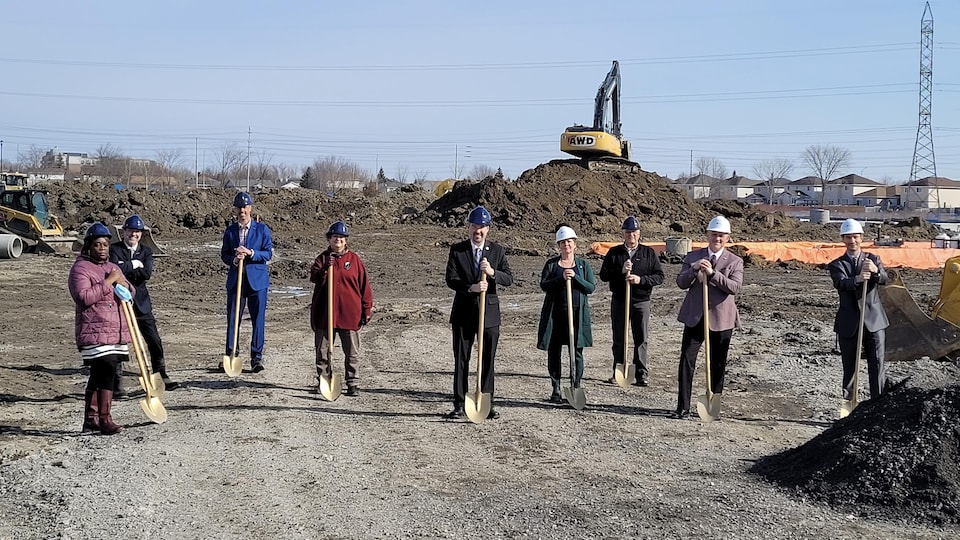 9 personnes qui tiennent des pelles sur un chantier de construction.