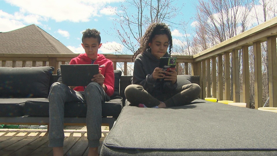 Deux enfants sont assis sur un balcon et tiennent un ordinateur portable.