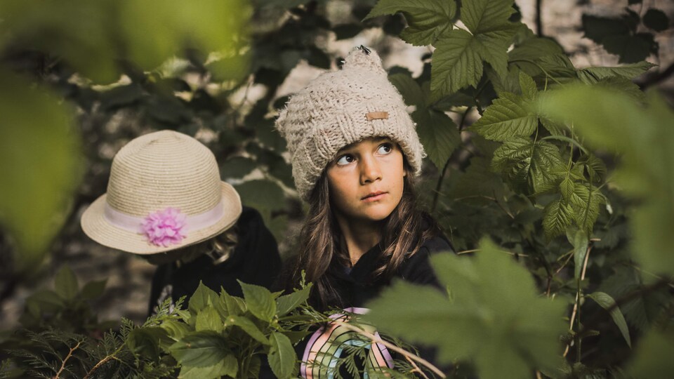 Deux enfants portant tuque et chapeau sont au milieu d'arbustes.