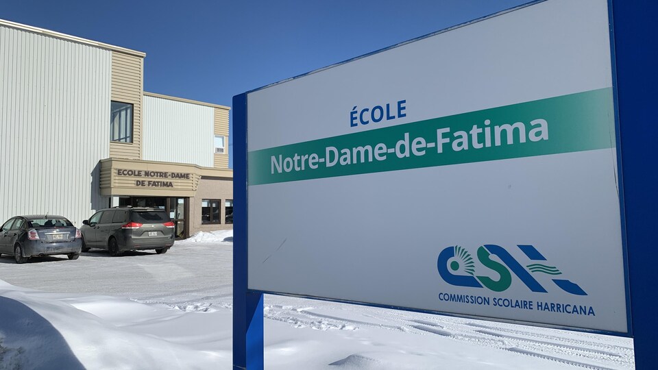 Des voitures sont stationnées devant l'établissement scolaire en hiver.