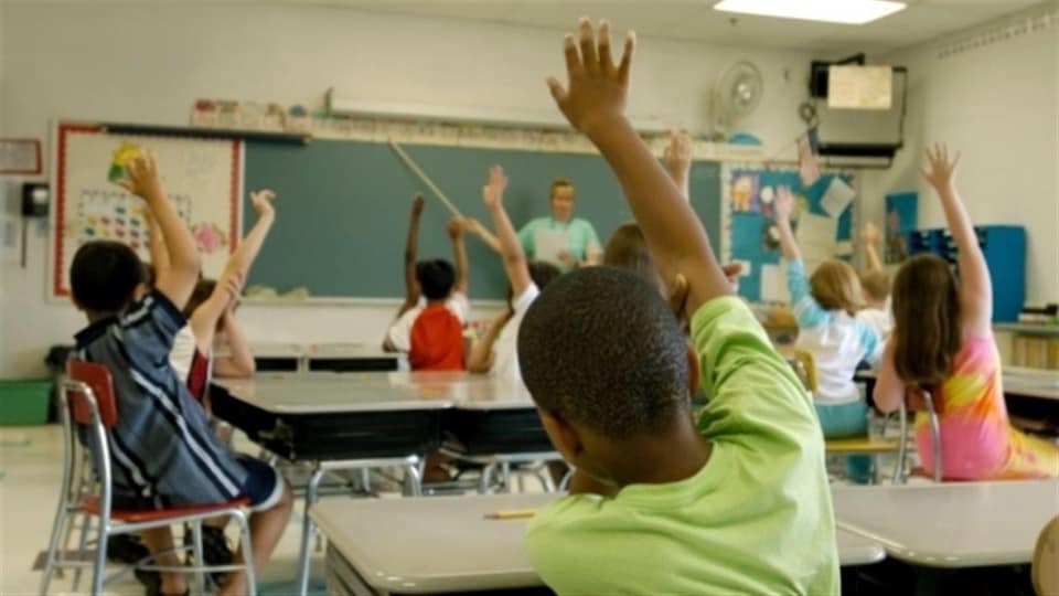 Des enfants assis sur leur chaise dans la classe lèvent la main 