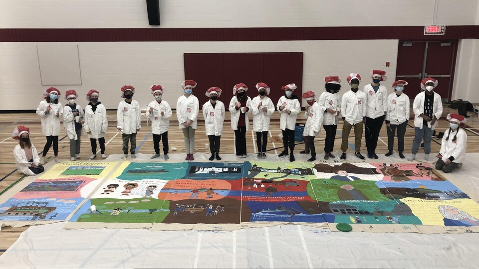 Les 18 jeunes dans leur tenue de peinture devant la toile étendue au sol.