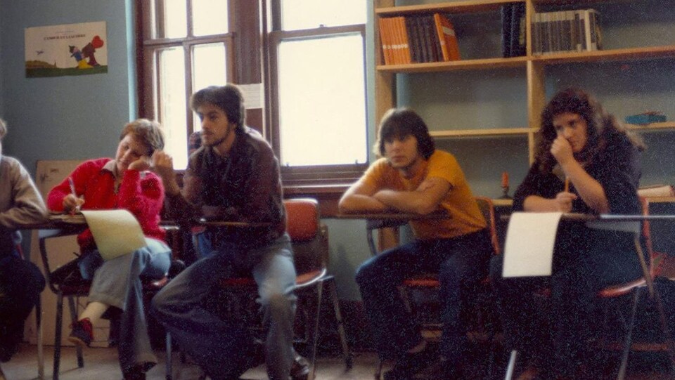 Quatre élèves assis à leur pupitre dans une salle de classe.