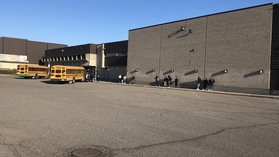 Des petits groupes d'élèves masqués se sont rejoints devant leur école secondaire.