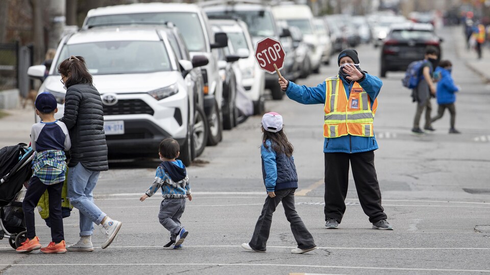 Des enfants traversent la rue en passant devant un brigadier scolaire.