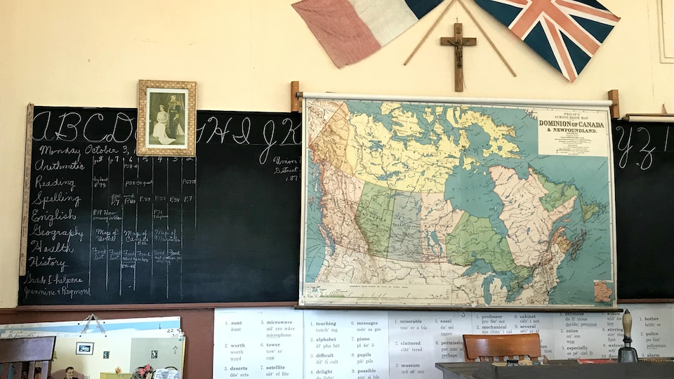 Le mur de l'école, où on peut voir d'anciens drapeaux, une ancienne carte du "Dominion du Canada" un tableau noir, et d'autres articles relatifs à la vie scolaire dans les débuts du 20e siècle. 