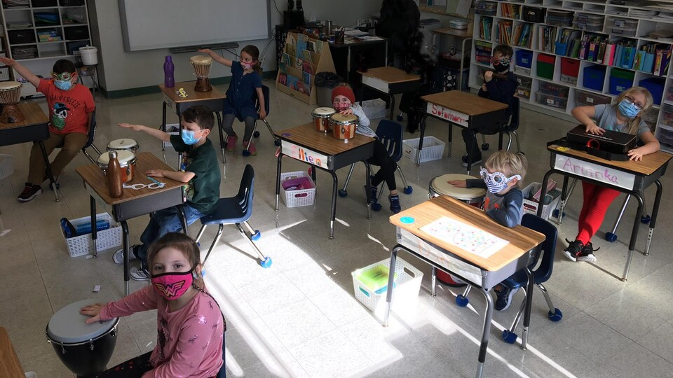 Des écoliers assis dans une classe qui jouent des instruments de percussion.