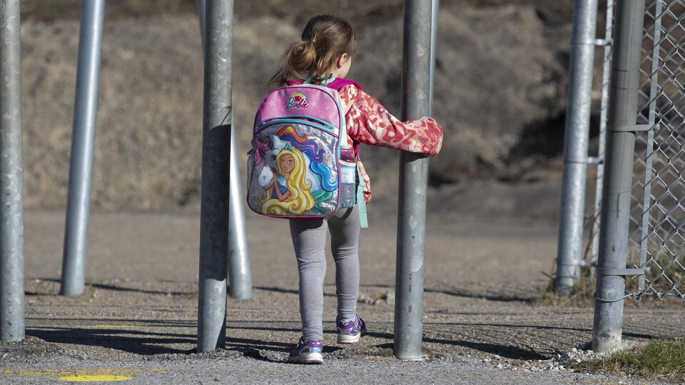 Une petite fille, de dos, portant un sac d'école.
