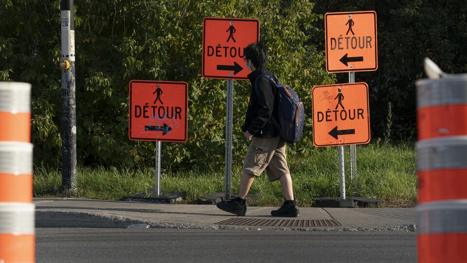 Un écolier marche près de pancartes indiquant des détours, mais dans des directions différentes.