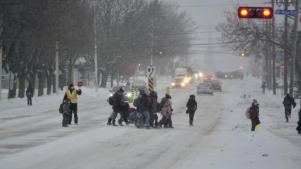 Des écoliers traversent la rue sous des précipitations de neige.
