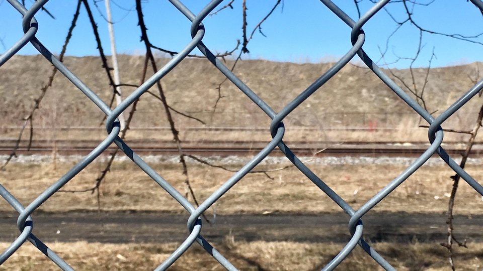 Le terrain contaminé appartenant à Ray-Mont Logistiques vu de l'autre côté d'une clôture de broche.