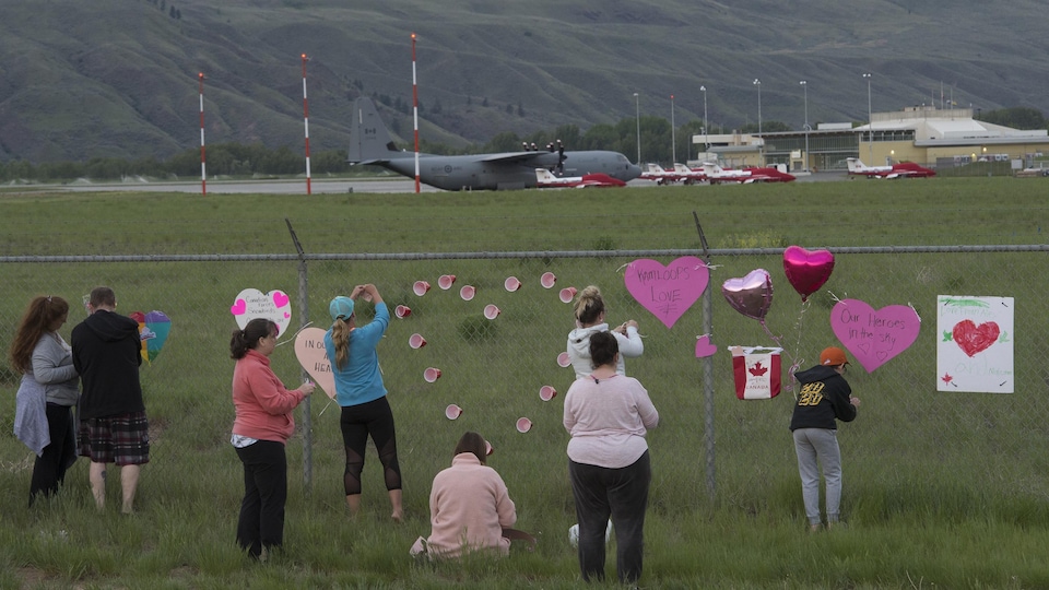 Des personnes accrochent des coeurs sur la clôture d'un aéroport.