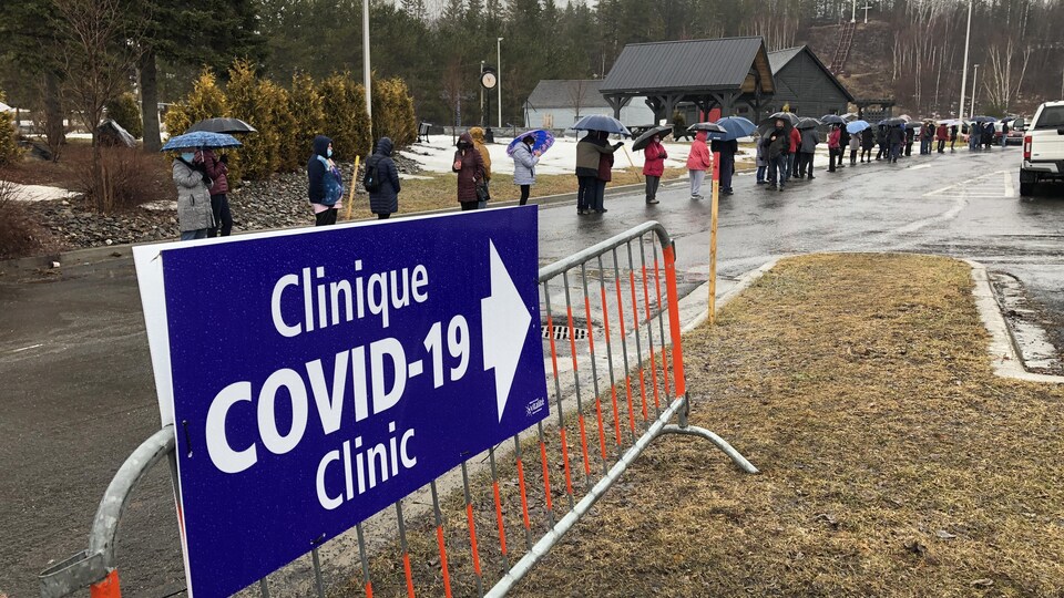 Des gens qui attendent en ligne sous la pluie.