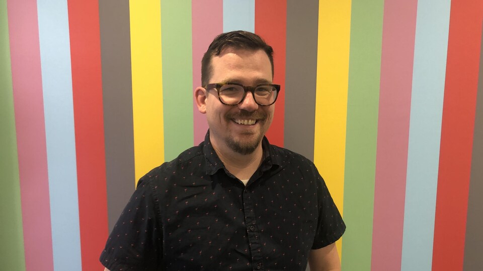 un homme sourit devant un mur coloré.