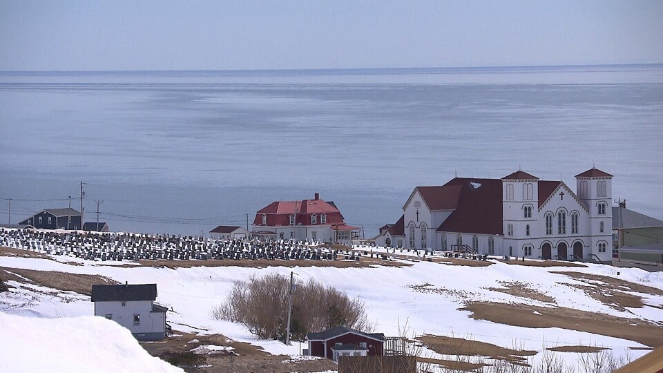 Le cimetière, l'église de Bassin et golfe du Saint-Laurent en hiver.