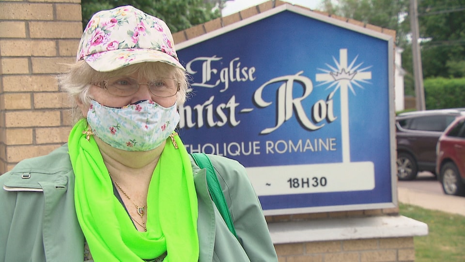 Réjeanne Cormier, une dame avec un masque protecteur en face de l'écriteau de l'église Christ-Roi