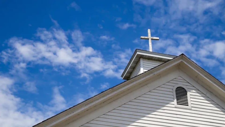 Le toit d'une église et sa croix sur fond de ciel.