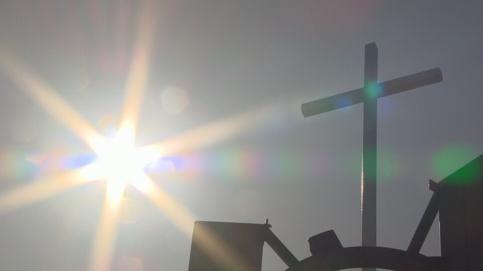 Photo du ciel avec le soleil. On y voit une croix qui fait partie du toit de la paroisse.