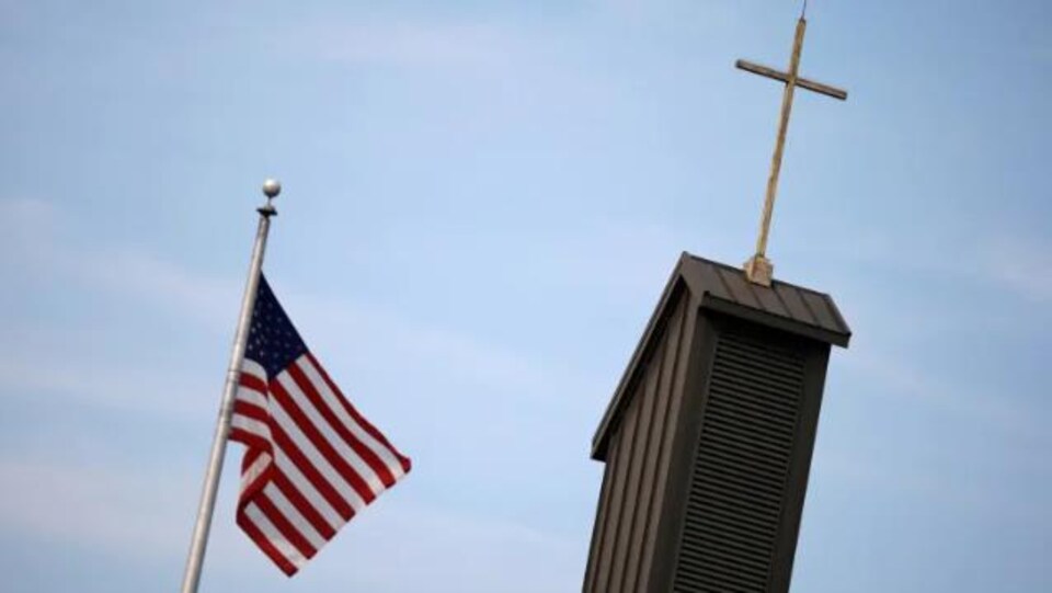 le drapeau des états-unis flotte dans les airs à côté de la croix de l'église cahtolique