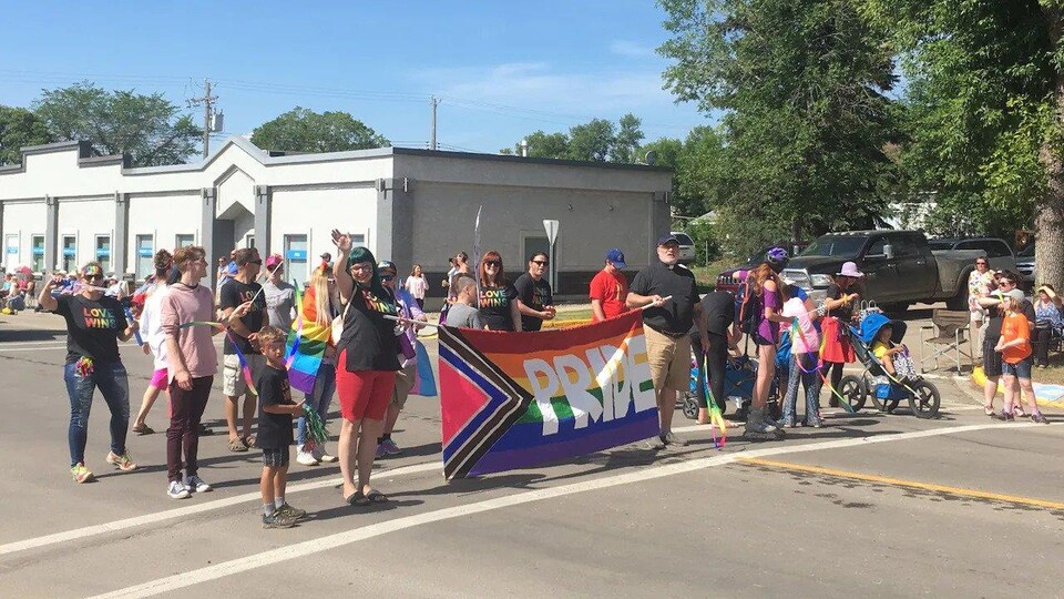 Des personnes marchent dans la rue en tenant un drapeau de la fierté gaie. 