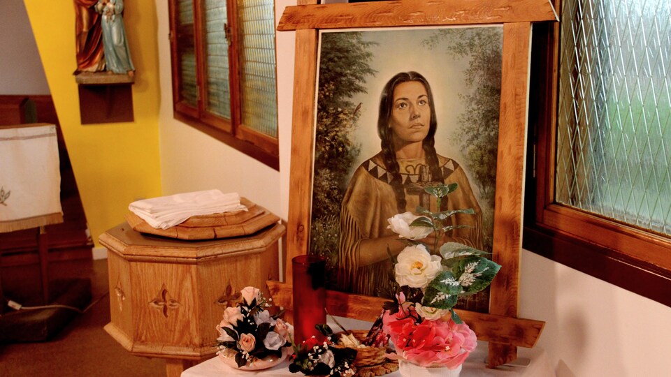 Une illustration d'une femme autochtone en train de prier posée sur une table de l'église devant laquelle des fleurs ont été déposées.
