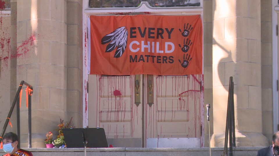 Façade de l'église recouverte de peinture rouge et avec un drapeau inscrit Every Child Matters.