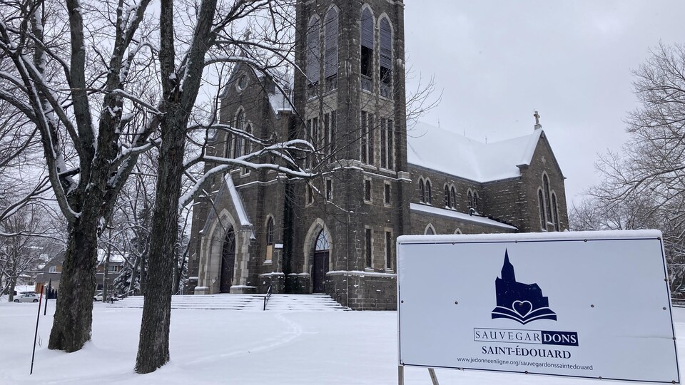 Une affiche du comité de sauvegarde plantée sur le terrain devant l'église en hiver.