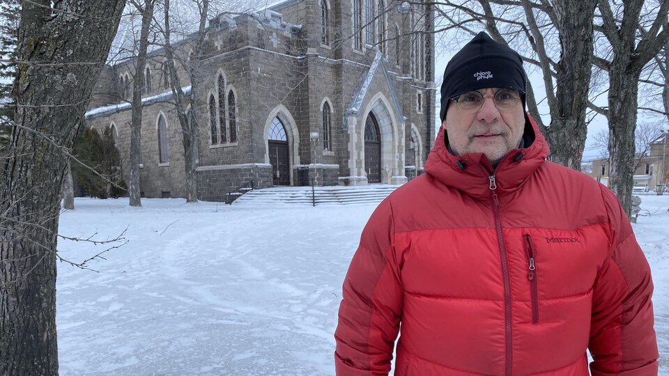 Un homme pose devant une église en hiver.