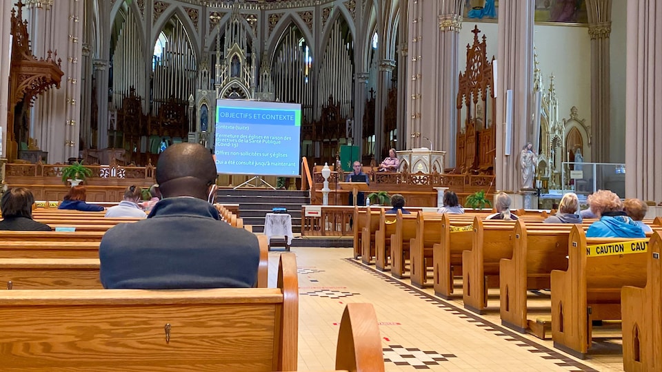 Des gens sont assis dans différentes rangées d'une église. À l'avant, une présentation Powerpoint est projetée sur une toile.
