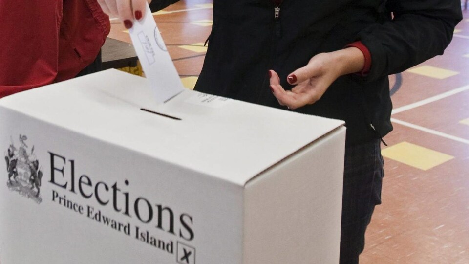 Une femme glisse un bulletin de vote dans la fente d'une boîte de scrutin.