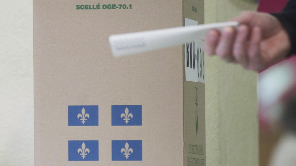 Un électeur dirige son bulletin de vote vers une boîte de scrutin.