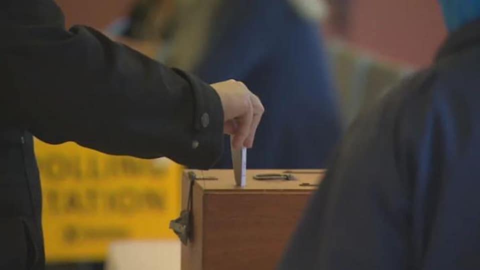 Une main déposant son vote dans la boîte. 